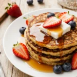 Sheet pan pancakes topped with syrup, butter, and berries on a wooden table.